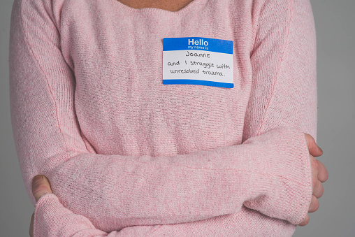 A single person in a studio wearing a nametag with a label about UNRESOLVED TRAUMA