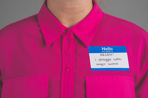 A single person in a studio wearing a nametag with a label about ANGER MANAGEMENT