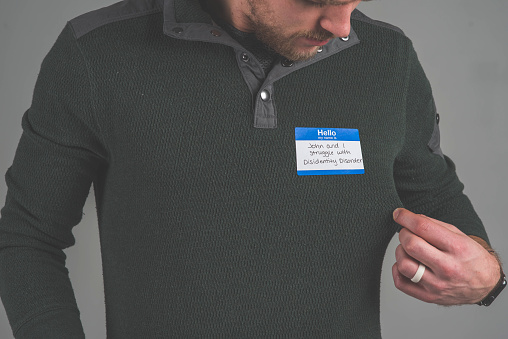 A single person in a studio wearing a nametag with a label about having a multiple personality disorder
