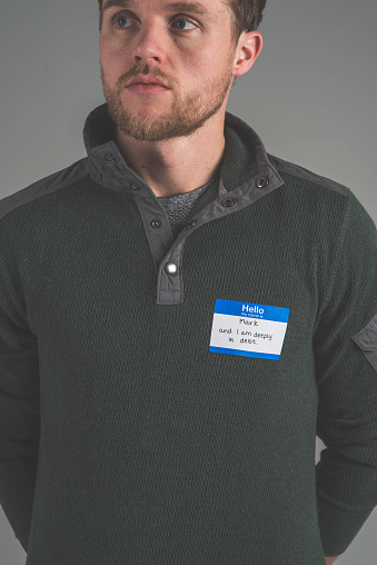 A single person in a studio wearing a nametag with a label about DEBT