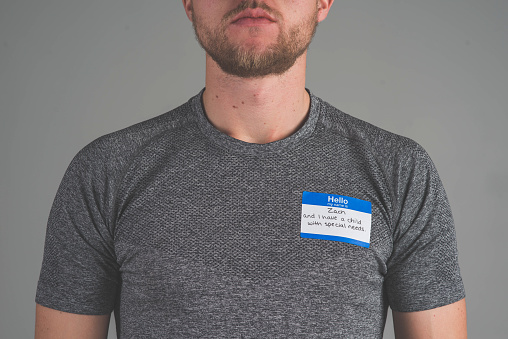 A single person in a studio wearing a nametag with a label about having a child with special needs