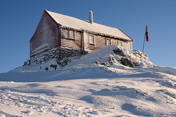 Red cabin at Christmas, in a snowy forest with the Hardanger Fjord in the background, in Norheimsund, Norway.