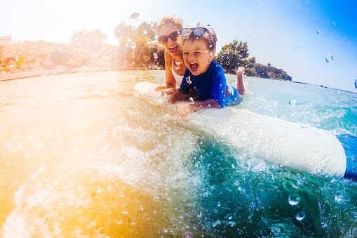 Photo of cute little boy and his mom floating on the surfboard in the sea