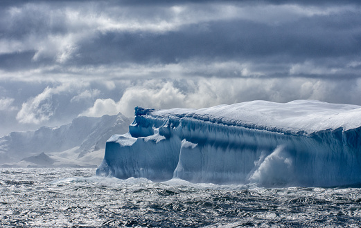 Massive Iceberg floating in the Southern Ocean in Antarctica with snow covered mountains in the background
