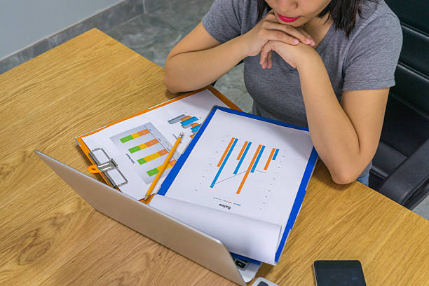 businesswoman reading reports with laptop and smartphone beside - research report document file imagens e fotografias de stock