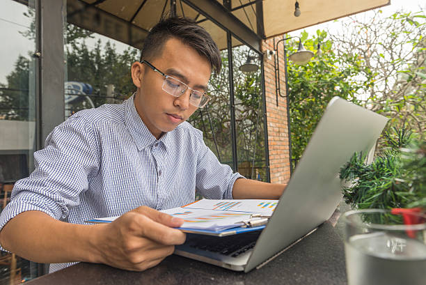 молодой бизнесмен работает с ноутбуком на открытом пространстве - research report document file стоковые фото и изображения