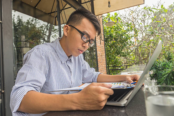 молодой студент-мужчина делает домашнее задание с ноутбуком на открытом воздухе - research report document file стоковые фото и изображения