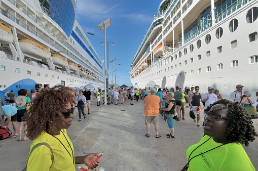 St. John's, Antigua and Barbuda - January 8, 2017: Two local tour guides meet the many cruise ships docked at St. John's in Antigua as passengers disembark onto Heritage Quay and get sorted out for the various shore excursions. The cruise ships form an urban like scene of high rises.