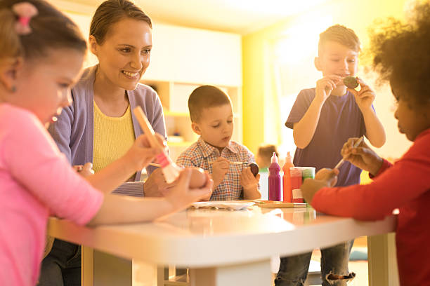 istock Smiling preschool teacher and children coloring Easter eggs together. 639679656