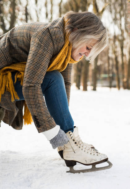 senior woman in winter clothes putting on old ice skates. - ice skates imagens e fotografias de stock