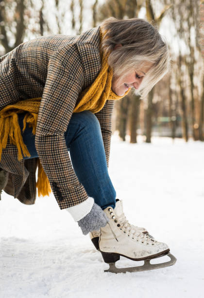 старшая женщина в зимней одежде надет старые коньки. - senior adult shoelace human leg leg стоковые фото и изображения