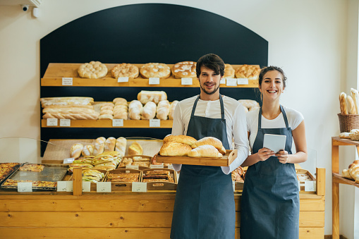 Two beautiful young bakers holding a tray of bread at the bakery.