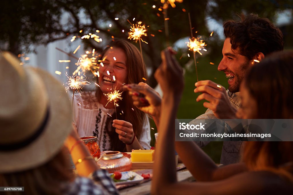 Friends With Sparklers Eating Food And Enjoying Party Meal Stock Photo
