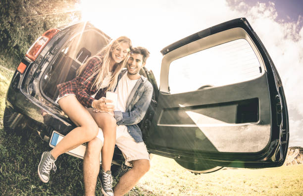 Young happy couple having fun with mobile phone at car