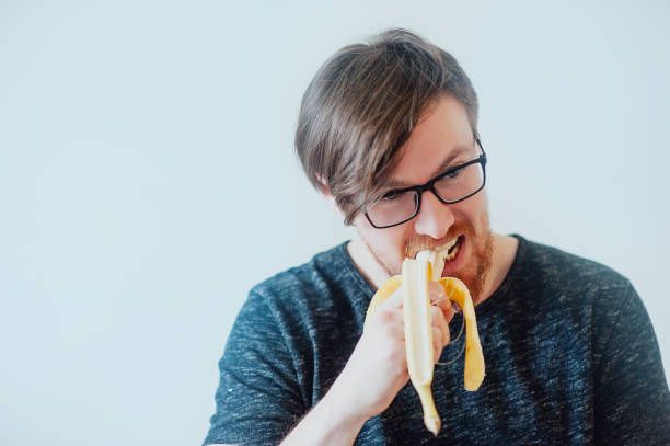 istock man with a beard wearing glasses eating  banana 639707712