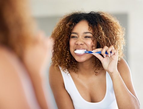 Shot of a young woman brushing her teeth in her bathroom