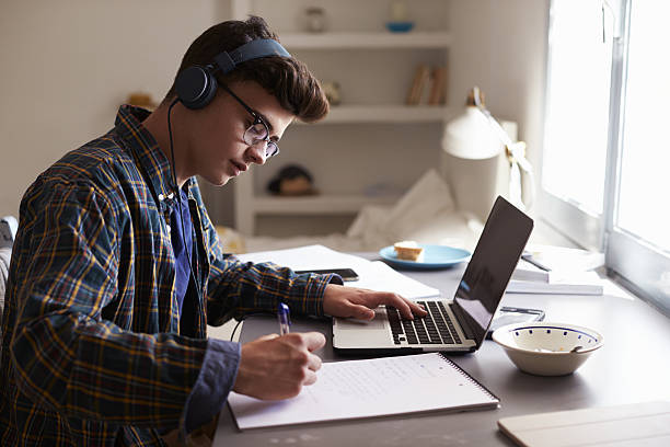 teenage boy wearing headphones works at desk in his bedroom - trabalho de casa imagens e fotografias de stock