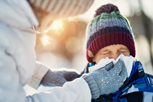 Mother and son having winter walk. Mother is blowing nose of her sick son.