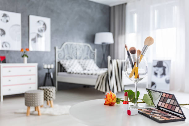 Szklanka wypełniona makijażem i kosmetyki na toaletce w stylowo urządzonej sypialni.
