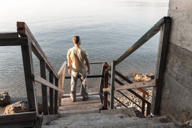 Young man stands on old wooden stairway going down to the sea coast