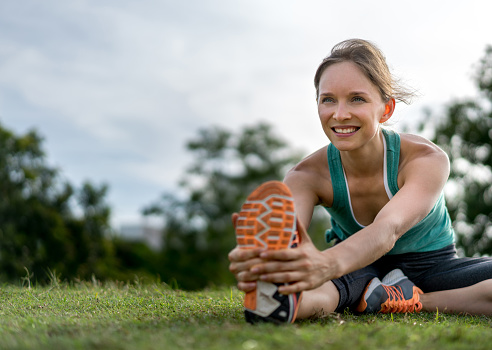 Portrait of a fit woman stretching at the park after her workout and looking very happy - women in sports concepts