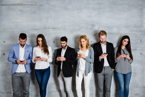 Group of business people standing against the wall and typing message on their smart phone