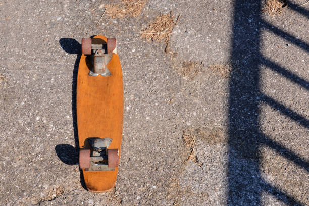 Skateboard is laying on the ground with its wheels off. The skateboard is old and has a wooden deck