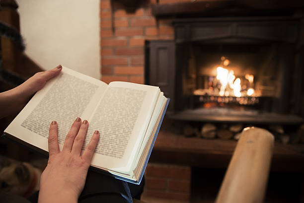 istock Woman reads book near fireplace,  resting with book 639735620