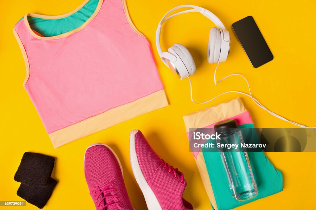 Fitness accessories on a yellow background. Sneakers, bottle of water Fitness accessories on a yellow background. Sneakers, bottle of water, earphones and sport top. Still life Active Lifestyle Stock Photo