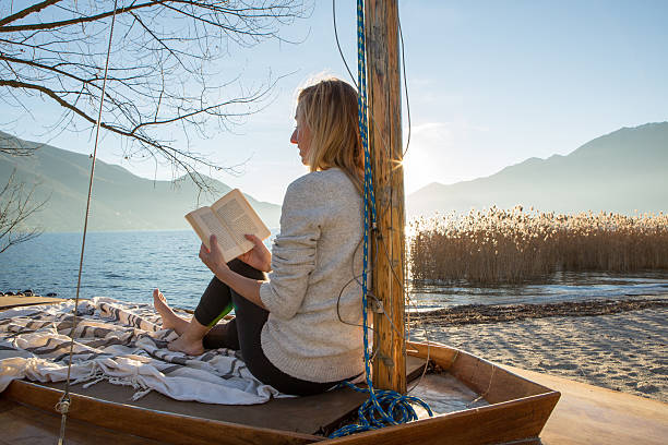 istock Young woman relaxing by the lake reading book 639739488