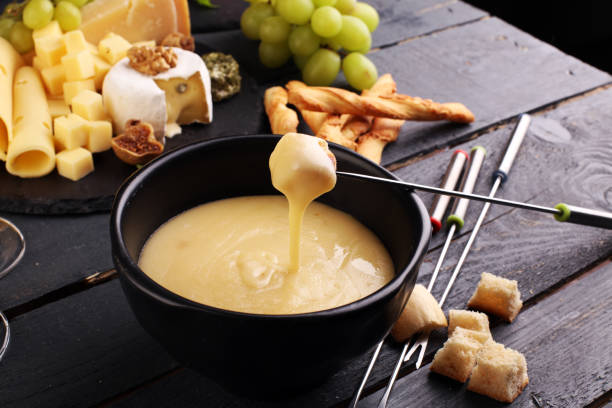 Gourmet Swiss fondue dinner Gourmet Swiss fondue dinner on a winter evening with assorted cheeses on a board alongside a heated pot of cheese fondue with two forks dipping bread and white wine behind in a tavern or restaurant melting photos stock pictures, royalty-free photos & images