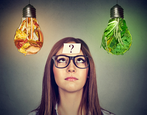Woman in glasses question mark on head thinking looking at junk food and green vegetables light bulb isolated on gray background.
