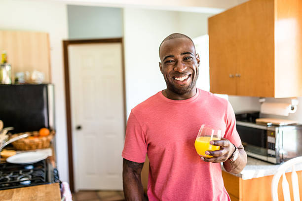 uomo africano sorridente bere succo d'arancia - juice glass healthy eating healthy lifestyle foto e immagini stock