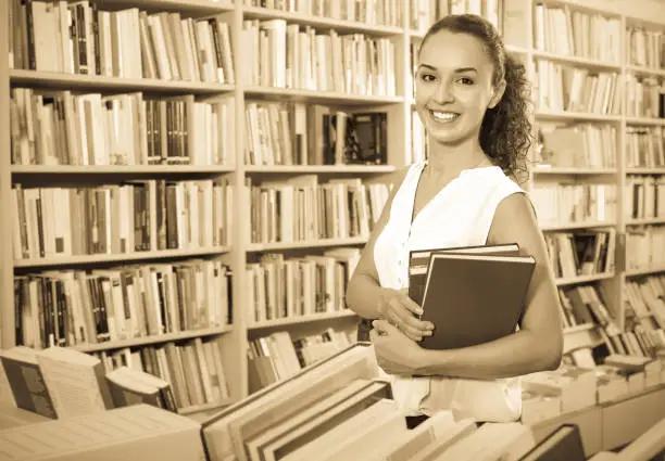Young  positive woman buying books in hard cover in bookstore