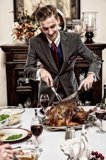 1940's Father Figure dressed in his suit and tie, cutting a roasted turkey at a table set for dinner for his family.  Goblets of wine, peas, Mashed potatoes and gravy are spread out across the table. The picture behind him has been altered then blurred.   1/4 of the image is showing.  It has been altered and blurred beyond recognition.