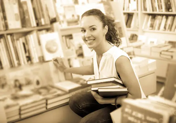 Positive glad woman taking literature books in store with prints