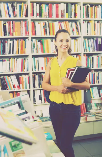Portrait of smiling young woman choosing textbooks for school in book shop