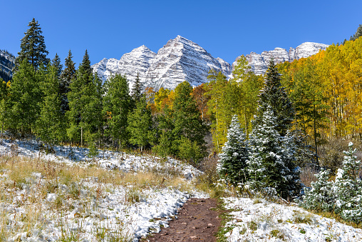 A hiking trail extending toward snow covered Maroon Bells. Aspen, Colorado, USA.