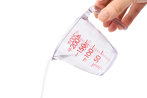 Close-up of pouring water from measuring cup, isolated on white background with clipping path.