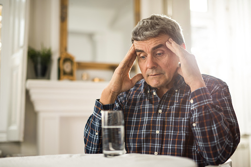 Senior man sitting at home and holding his head in pain.