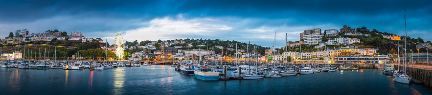 The hotels and villas, quayside shops, pubs and restaurants of Torquay overlooking the yachts in the harbour marina illuminated at dusk, in the heart of the English Riveria, Devon, UK.