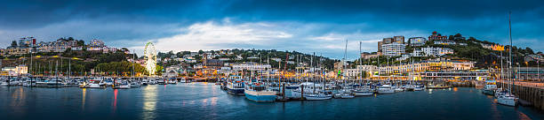Yachts moored in Torquay harbour marina English Riveria panorama Devon The hotels and villas, quayside shops, pubs and restaurants of Torquay overlooking the yachts in the harbour marina illuminated at dusk, in the heart of the English Riveria, Devon, UK. torquay uk stock pictures, royalty-free photos & images