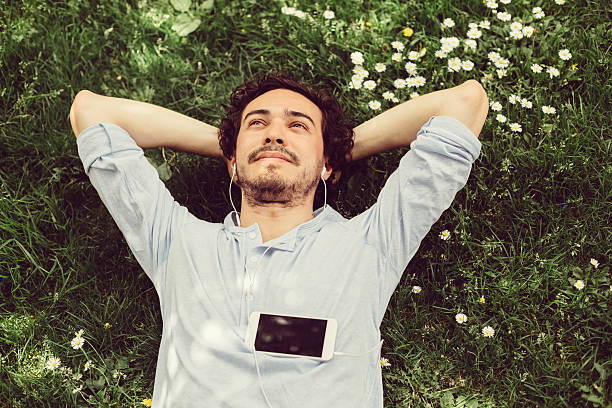 Dreamy man in the grass Young man relaxing in the grass and enjoying the music serene people stock pictures, royalty-free photos & images
