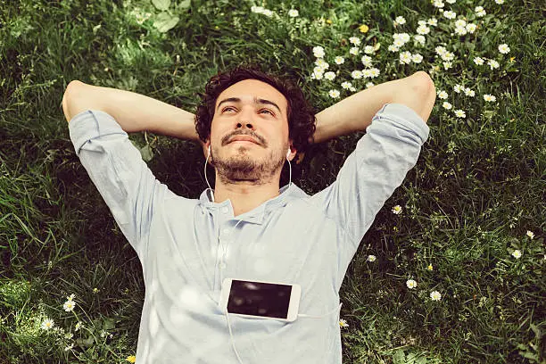 Young man relaxing in the grass and enjoying the music