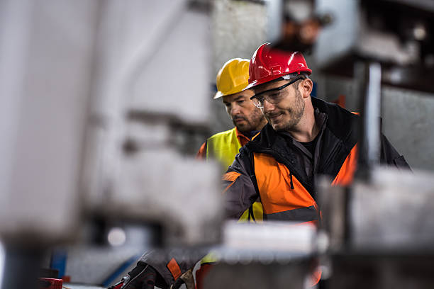 Metal workers cooperating while working in aluminum mill. Two manual workers standing in a aluminum mill and working together. Focus is on man with red hardhat. manufacturing occupation stock pictures, royalty-free photos & images