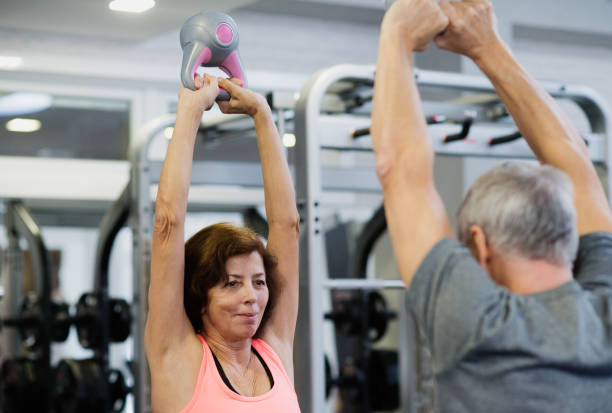 Senior couple in gym working out using kettlebells. Beautiful fit senior couple in gym working out using kettlebells. senior bodybuilders stock pictures, royalty-free photos & images
