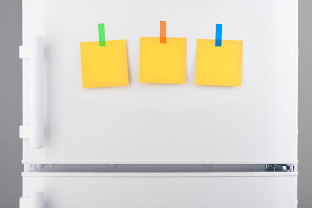 istock Yellow paper notes attached with stickers on white refrigerator 639811462