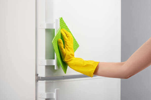 istock Hand in yellow glove cleaning white refrigerator with green rag 639811876