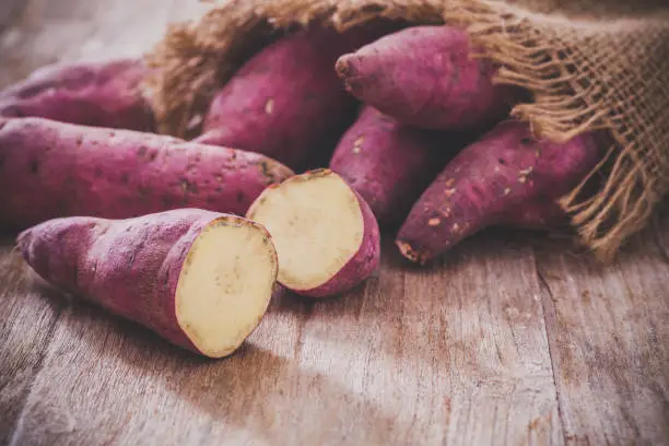 Raw sweet potatoes on wood background