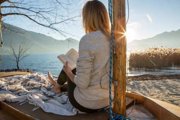 istock Young woman relaxing by the lake reading book 639842302